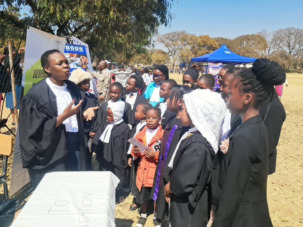 A JCC facilitator in a black gown addresses a group of student participants at the Right to Education table