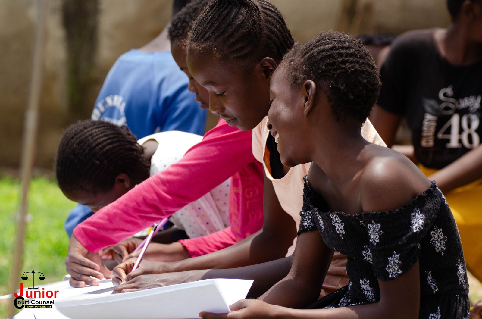 Three girls leaning in together to write on the same sheet of paper during a JCC workshop